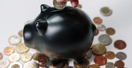 A human hand placing a coin into a piggy bank.