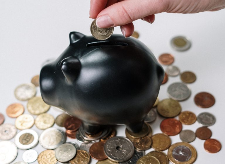 A human hand placing a coin into a piggy bank.